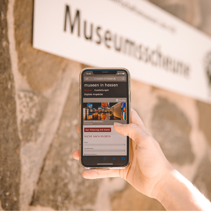 Mobile Ansicht der Website Museen in Hessen auf einem Smartphone vor einer Steinmauer.