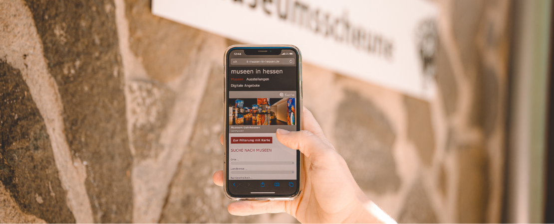 Mobile Ansicht der Website Museen in Hessen auf einem Smartphone vor einer Steinmauer.