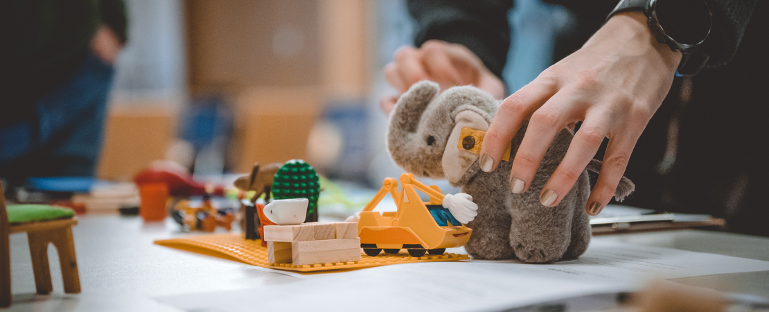 Planspiel aus Legobausteinen, Spielzeugen und einem Plüschelefant der von einer Hand platziert wird.