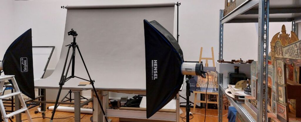 Ein aufgebautes Fotostudio mit Stativ und Blenden für Aufnahmen. Rechts stehen Papiertheater-Objekte in einem Schwerlastregal.