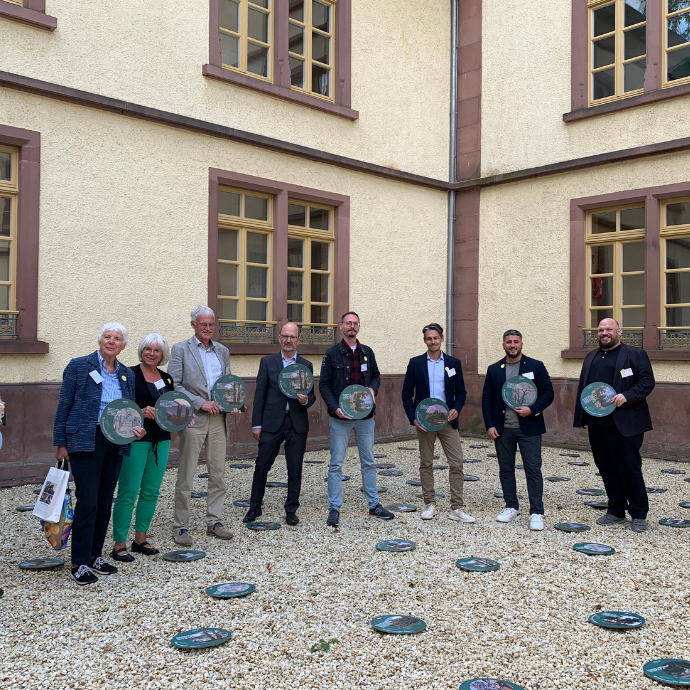 Gruppenbild, alle halten eine stilisierte Baumscheibe in der Hand, Teilnehmende des Energie-Check 2022 beim Verbandstag 2023 im Innenhof des Michelstaedter Stadthauses.