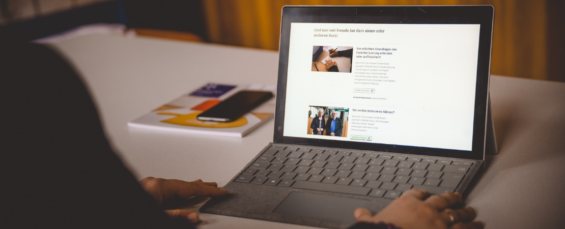 Eine Person sitzt an einem Laptop und hat die Website der Selbstlernkurse des Museumsverbandes Hessen geöffnet.