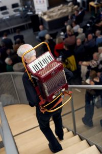 Der Künstler Axel Kretschmer geht auf einer Treppe hinunter und trägt auf dem Rücken ein Akkordeon.