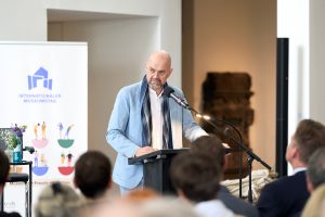 Dr. Dirk Pörschmann am Rednerpult bei seinen Grußworten anlässlich der Veranstaltung. Im Hintergrund ein Banner des Internationalen Museumstags.