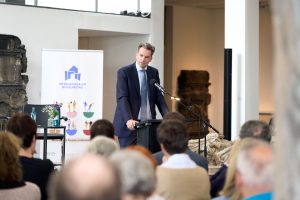 Dr. Sven Schoeller am Rednerpult bei seinen Grußworten anlässlich der Veranstaltung. Im Hintergrund ein Banner des Internationalen Museumstags.