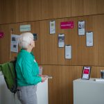 Blick auf die Pop-Up-Ausstellung, die den Verbandstag 2024 begleitete. Eine Teilnehmerin Schaut sich die Beispiele der Social Media-Kampagne #DateImDepot. An einer Wand sind Karten in Form eines Smartphones angebracht, die Beispiele für Objektinszenierung bei Social Media präsentieren. Vor der Wand befindet sich eine Steele, auf der ein Tablet weitere Beispiele präsentiert.