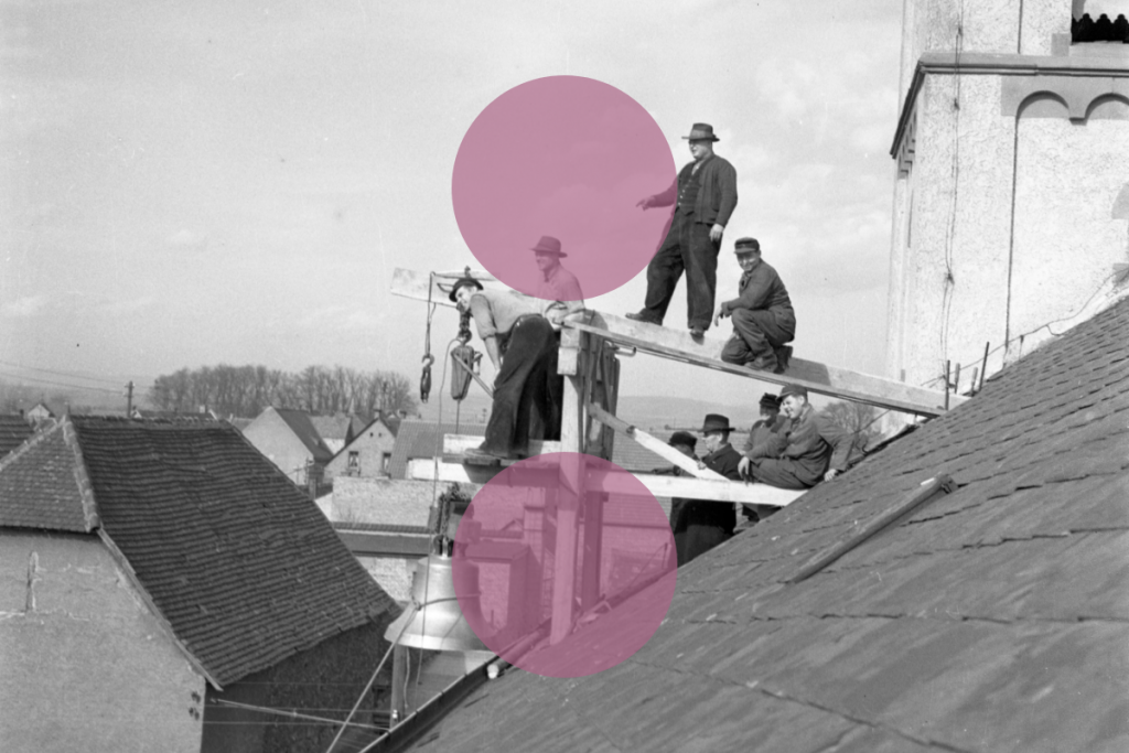 Historische Szene einer Gruppe von Männern, die auf einem Dach arbeiten, vermutlich bei der Installation einer Glocke. Einige tragen Hüte, während ein Arbeiter ein Seil hält. Im Hintergrund erstreckt sich eine ländliche Dorflandschaft. Zwei rosa Kreise überdecken mittig und unten Teile des Bildes.