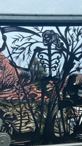 Nahaufnahme einer Glasbrücke mit Scherenschnitt. Es ist eine nackte Frau in einer natürlichen Umgebung zu sehen. Die Frau hält die Hand eines Skelett. Dieses rennt in die andere Richtung.