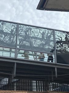 Nahaufnahme einer Glasbrücke mit Scherenschnitt. Es ist eine nackte Frau in einer natürlichen Umgebung zu sehen. Die Frau hält die Hand eines Skelett. Dieses rennt in die andere Richtung.