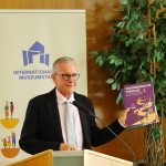 Bürgermeister Mario Schramm steht hinter einem Stehpult und hält die Publikation "Stadtgeschichte für Eilige" in der Hand. Dahinter ist das Banner zum Internationalen Museumstag sowie rechts daneben eine große Topfpflanze zu sehen.