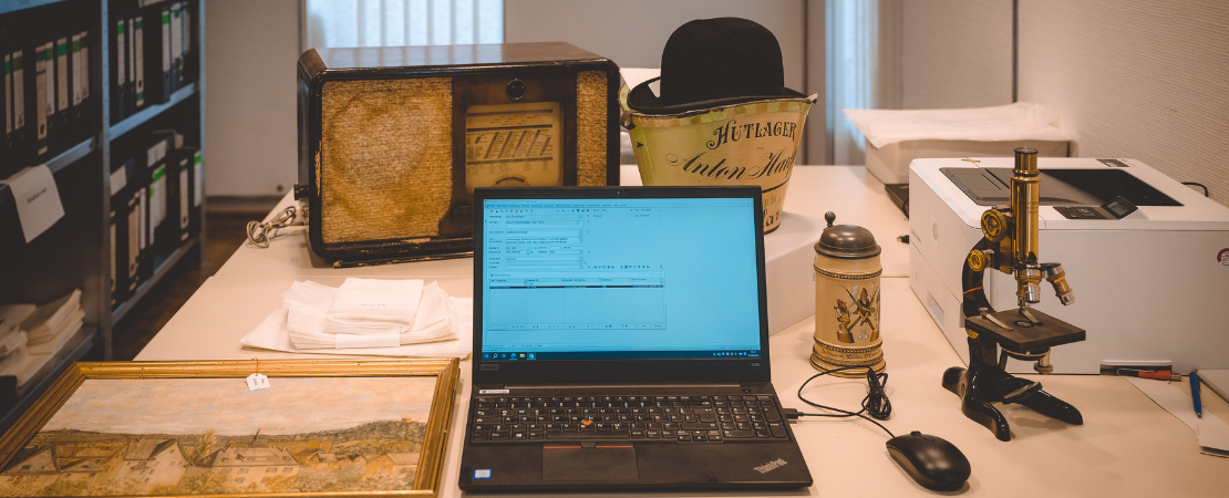 Notebook aufgeklappt neben Objekten eines Museums auf einem Tisch