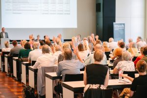 Die Mitgliederversammlung des Museumsverbandes Hessen e.V. entlastet den Vorstand. Handzeichen, Publikum von hinten fotografiert.
