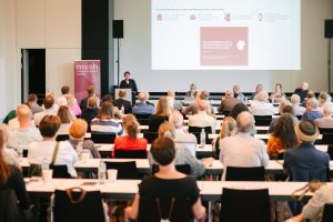 Blick in den Saal, Publikum von Hinten, Vorne Dr. Birgit Kümmel vor Präsentation