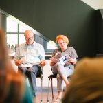 Ein Mann und eine Frau sitzen in einem Stuhlkreis und blättern jeweils in einer Broschüre.