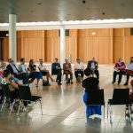 Gruppe von Personen sitzt in einem hellen Raum im Stuhlkreis und nimmt an einer Gesprächsrunde teil.