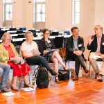 Gruppe von Personen sitzt in einem hellen Raum im Stuhlkreis und nimmt an einer Gesprächsrunde teil.