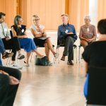 Gruppe von Personen sitzt in einem hellen Raum im Stuhlkreis und nimmt an einer Gesprächsrunde teil.