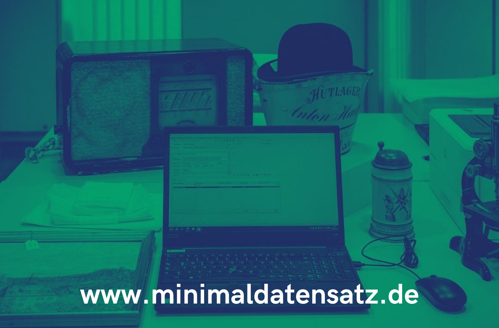 Grün eingefärbtes Bildmotiv. Schreibtisch Arbeitsplatz der digitalen Sammlungserfassung mit Notebook und Objekten darunter ein Krug. Unten: www.minimaldatensatz.de