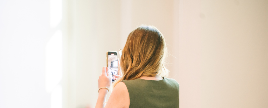 Person fotografiert mit dem Smartphone in einem hellen, minimalistischen Innenraum oder Ausstellungsraum.