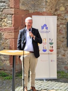 Oberbürgermeister Patrick Burghard steht mit Blick Richtung Kamera hinter einem Stehtisch und hält ein Mikrofon in der Hand; im Hintergrund ist die Festungsmauer sowie das Banner zum Internationalen Museumstags.