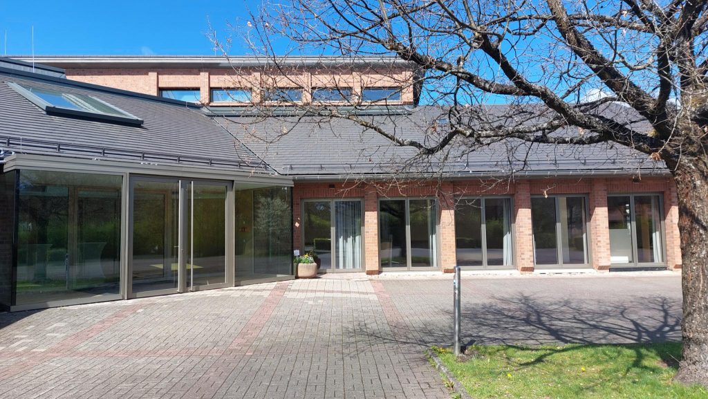 Philipp Soldan Forum Außenansicht, Rechts im Vordergrund ein Baum, blauer Himmel, ein Gebäude mit Dach und Glasfronten