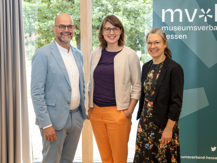 Dirk Pörschmann, Katharina Weick-Joch und Ulrike Sbresny stehen nebeneinander vor einem Fenster und einem Banner des Museumsverbands Hessen und blicken in die Kamera.