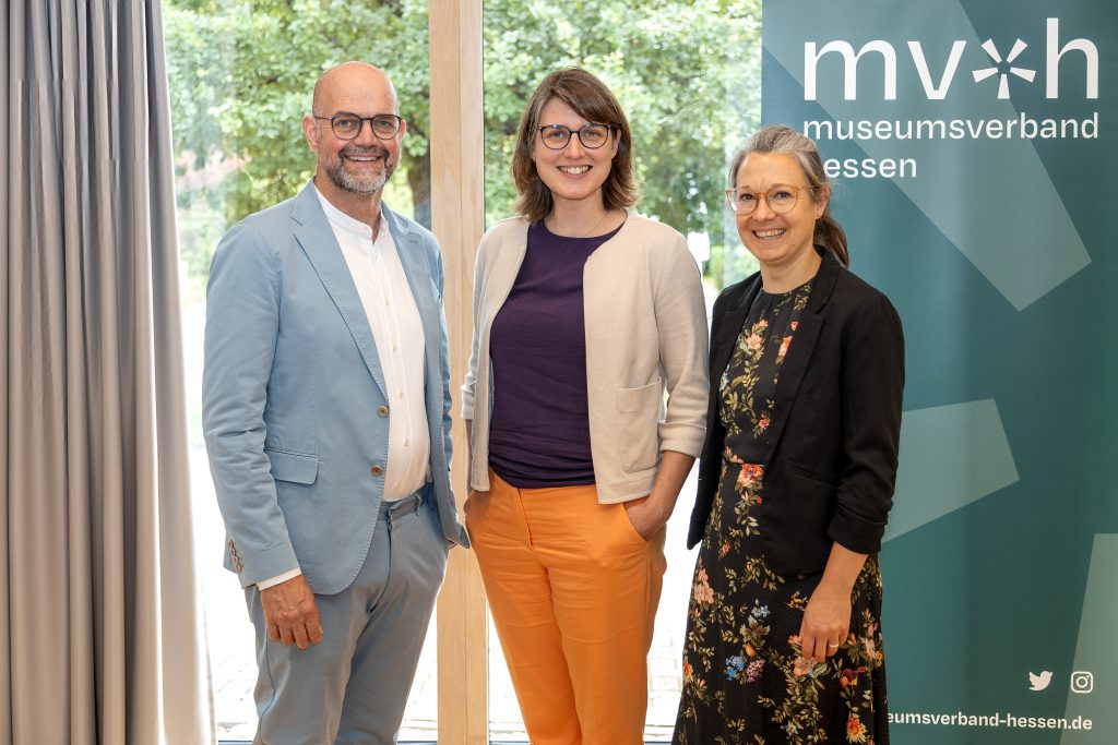 
Dirk Pörschmann, Katharina Weick-Joch und Ulrike Sbresny stehen nebeneinander vor einem Fenster und einem Banner des Museumsverbands Hessen und blicken in die Kamera. 