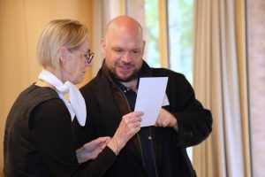 Eine Frau mit Brille und weißem Halstuch betrachtet gemeinsam mit einem Mann ein Dokument. Der Mann zeigt mit dem Finger auf etwas auf dem Dokument.