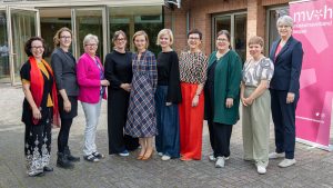 Das Team des Museumsverbandes Hessen steht nebeneinander vor einem Gebäude und lächelt in die Kamera. Rechts steht ein Aufsteller mit Logo.